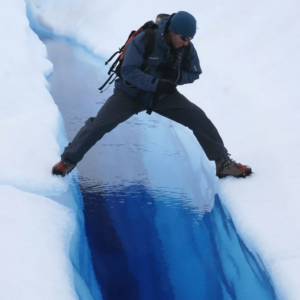 Hiker straddling a deep blue glacier crevasse, a metaphor for avoiding pitfalls