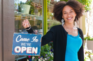 Small business owner holding a come in sign outside her shop