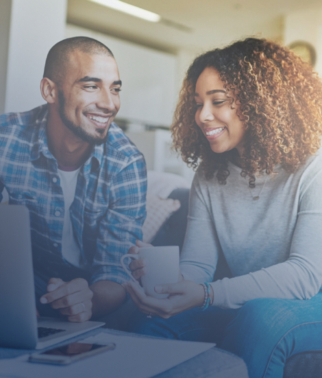 Two smiling credit union members looking at a laptop together over coffee