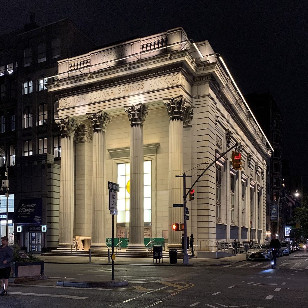 The Union Square Savings Bank building in New York at night, with its four tall Corinthian columns lit from below